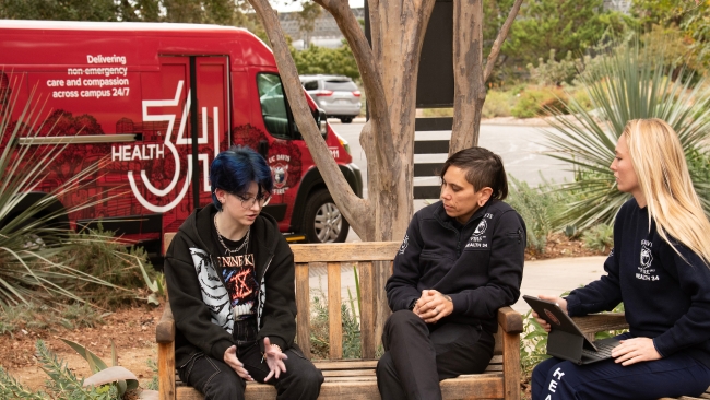 A student talks to two professionals with the University of California, Davis, Fire Department on a bench in front of a red van