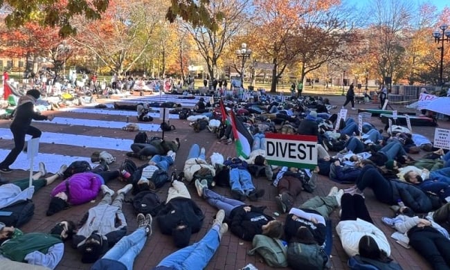 University of Michigan students protest for divestment, lying on the group and holding up a sign in the colors of the Palestinian flag that says, "Divest."
