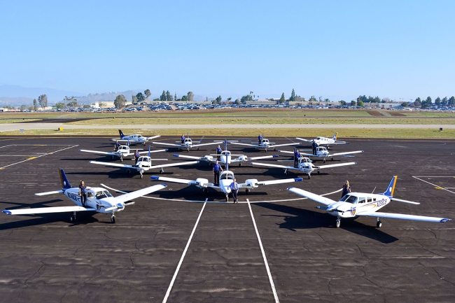 Students pose on the wings of small airplanes at California Baptist University's flight facility near Riverside, Calif.