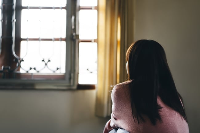 Rear view of young Asian woman lonely and tired sitting near window