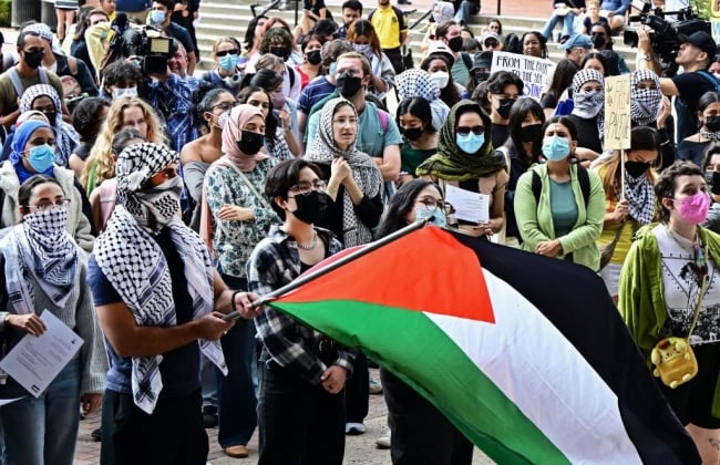 A student at UCLA waves a Palestinian flag with protesters in the background. 