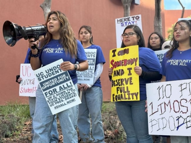 A group of undocumented students hold protest signs. One yells into a bullhorn.