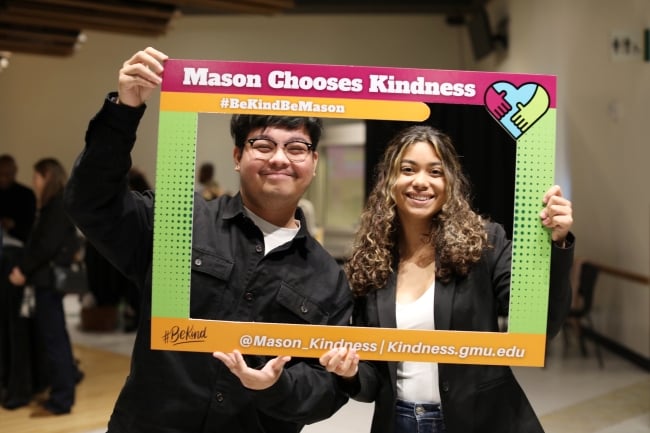 Two students pose in black-and-white business attire inside a photo frame that says Mason Chooses Kindness
