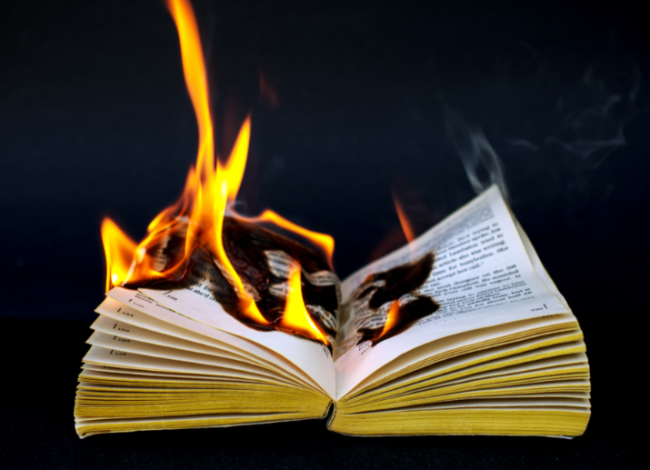 An open book, on fire, against a black background.