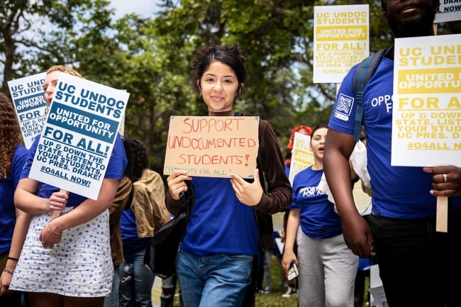 Students in blue shirts hold protest signs calling for support of undocumented students