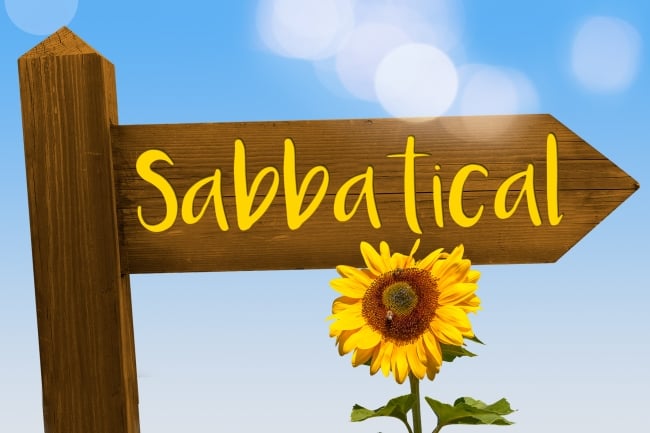 Sign reading Sabbatical pointing to the right with a flower underneath it