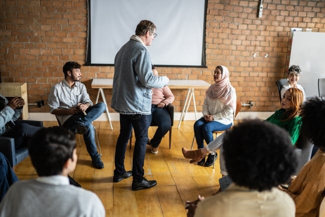 A professor stands in the middle of a circle of students, giving a lesson. 