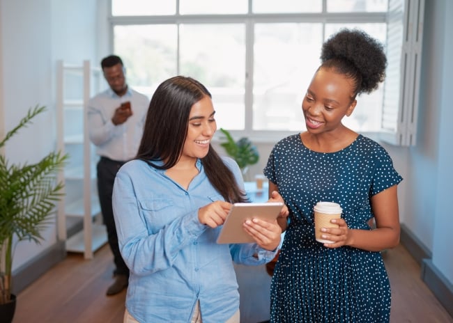 Two businesswomen talk in the office with digital tablet