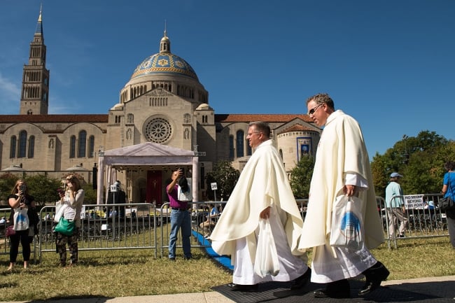 Two clergymen walk in front of the National Shrine of the Immaculate Conception and the Catholic University of America campus.