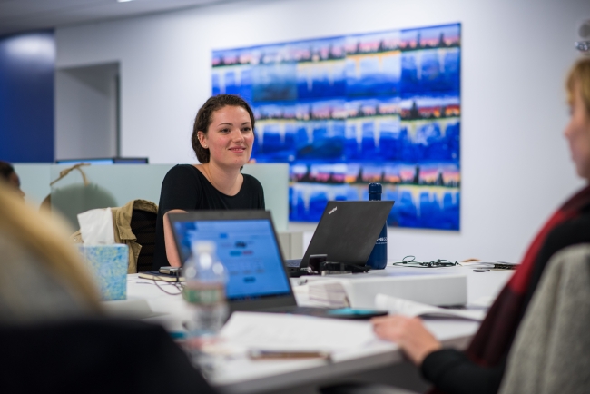 Young woman smiles and looks up from her laptop at a colleague in a shared office space. 