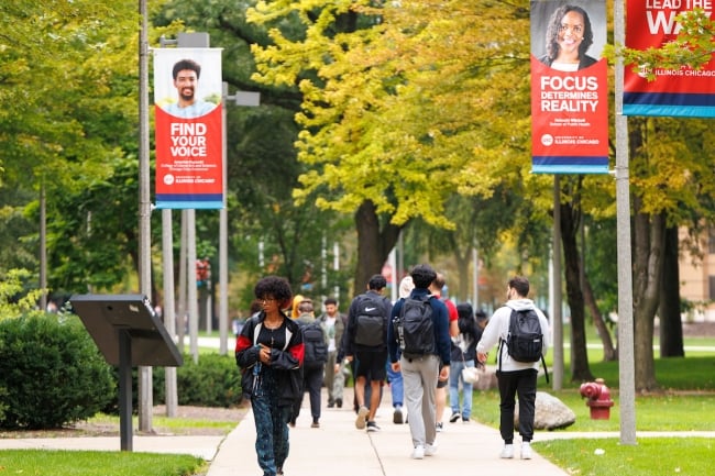 Students walk down a treelined sidewalk on campus