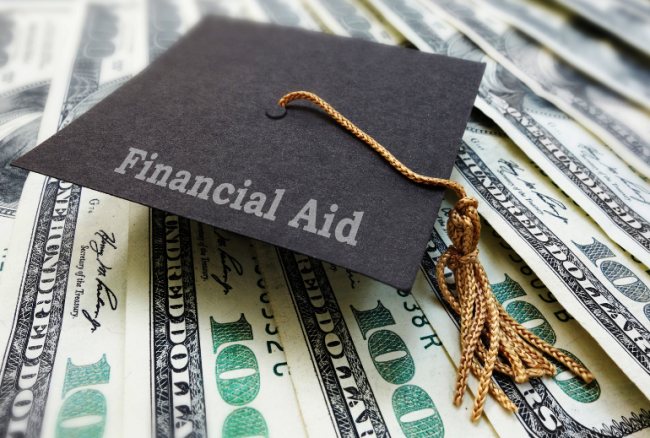 A graduation cap with the words "Financial Aid" sits atop a pile of $100 bills.