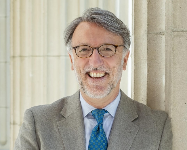 A man in glasses and a suit with blue tie smiling