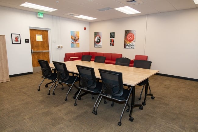 A photo of Sacramento State’s Esak´timá Center interior, with a conference table, red couch and Native American art on the wall.