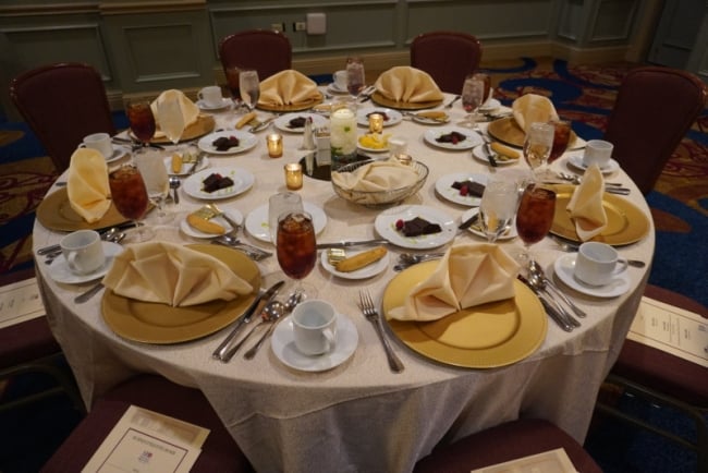 A formal dinner setting with multiple silverware, glasses and linen napkins