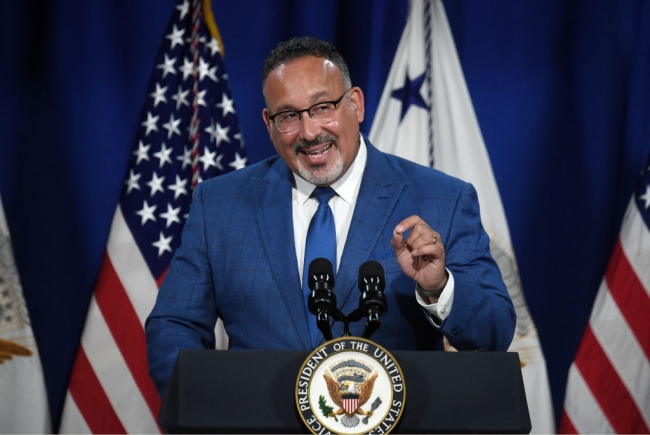 A man in a blue suit and tie at a podium in front of American flags