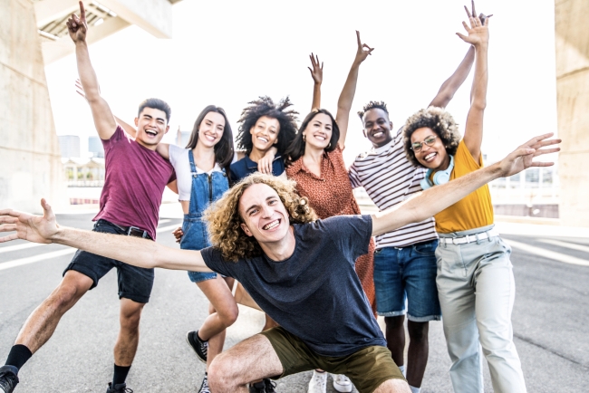 A big group of happy friends stands together with raised arms.