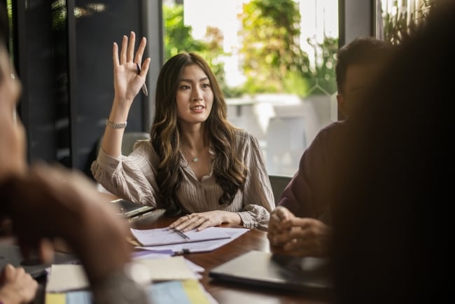 A woman raises her hand a classroom setting. 