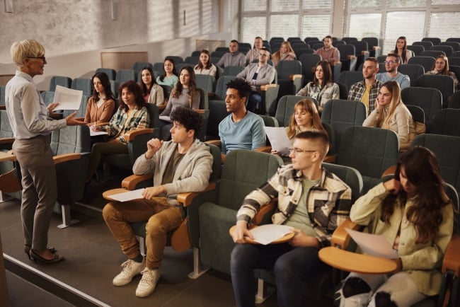 A side view of a female professor lecturing to college students in a classroom.