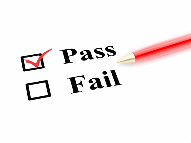 "Pass" is checked on a white paper with two options, "Pass" and "Fail." A red pen lies to the side.