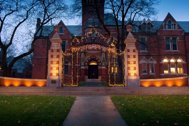 A photo of a building and gates on the Smith College campus adorned with holiday lighting.