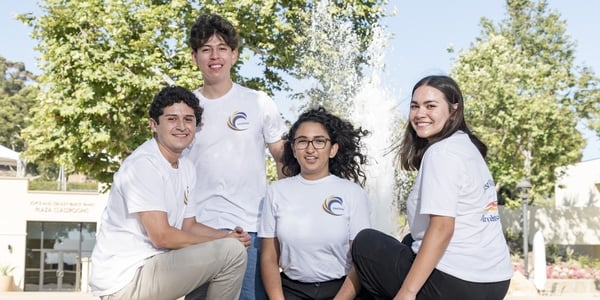 Four students pose in white T-shirts, facing the camera, in front of a fountain at Pepperdine University.