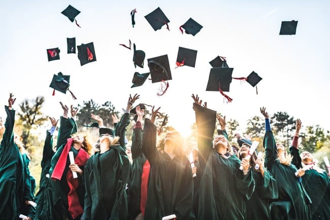 Students in graduation gowns throw their caps into the air.