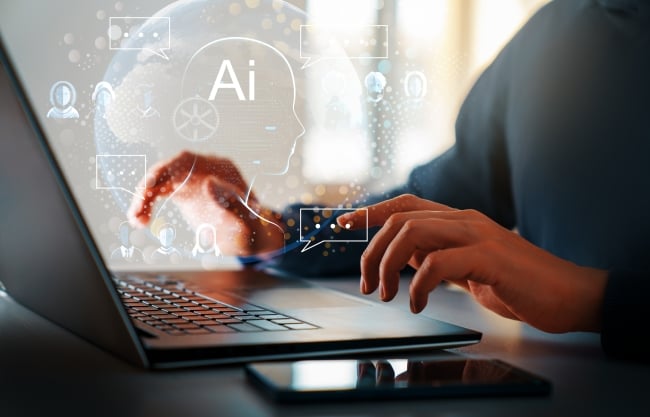 A close-up of a student’s hands on a laptop keyboard with icons relating to AI seeming to emanate from the computer.