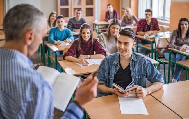 Man reading a book to a class in which students are smiling and engaged