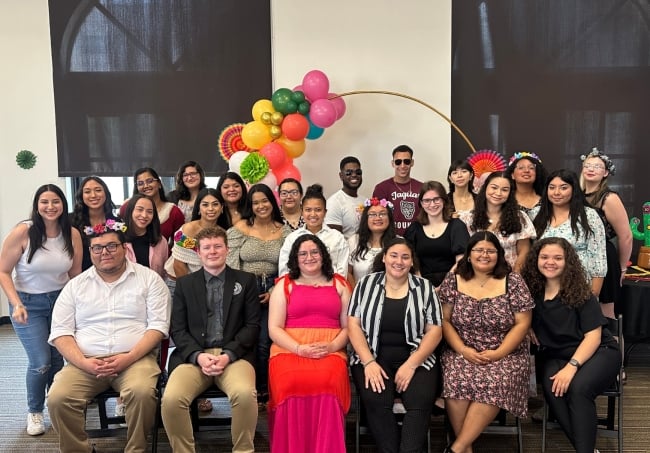 A group of students wearing dressy casual clothing smile for a photo 