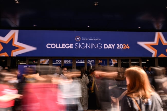 People moving in front of a sign that says College Signing Day