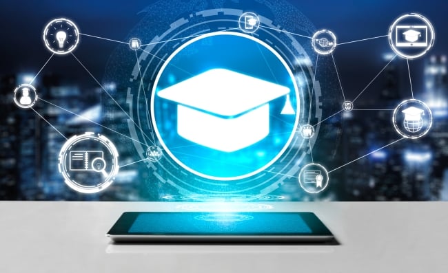 A tablet rests on a table and has a glowing, digitized graduation mortar cap above it