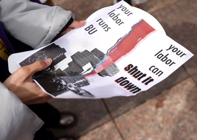 A student holds a flier with the words “your labor runs BU; your labor can shut it down.”
