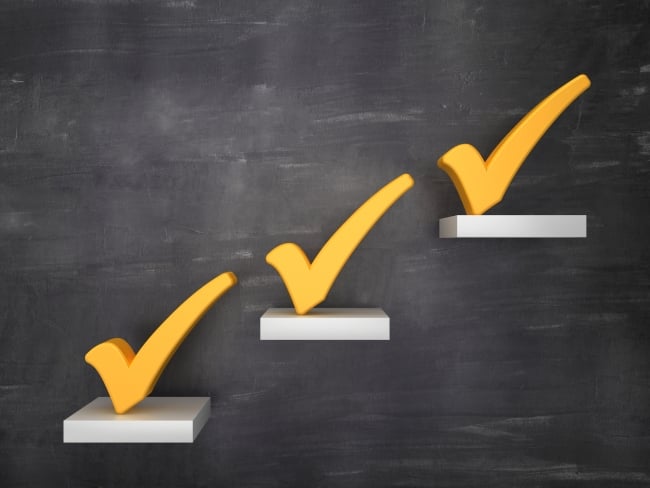 Three white steps going up toward the right on a dark wall with bright yellow checkmarks atop each.