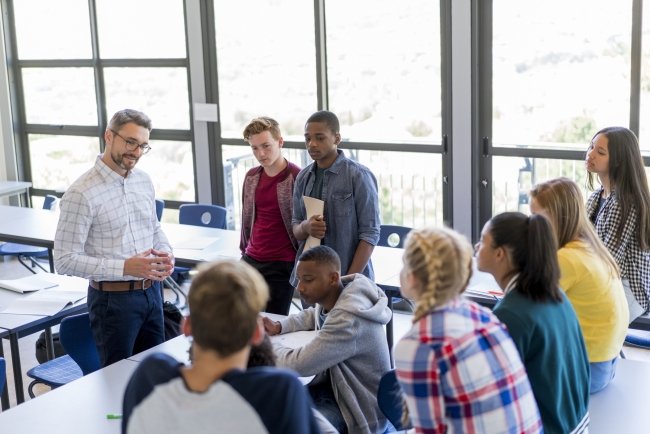 Multiethnic students and male teacher are discussing at school. They are casually dressed.