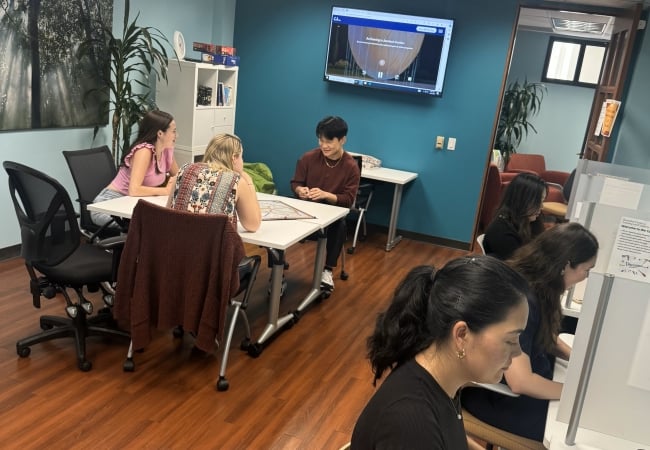 Students sit at computers and a group of students sits at a table together within the Kortschak Center for Learning and Creativity at USC.