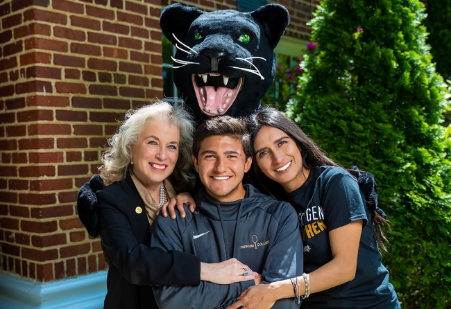 Three people pose for a photo with a panther mascot above them