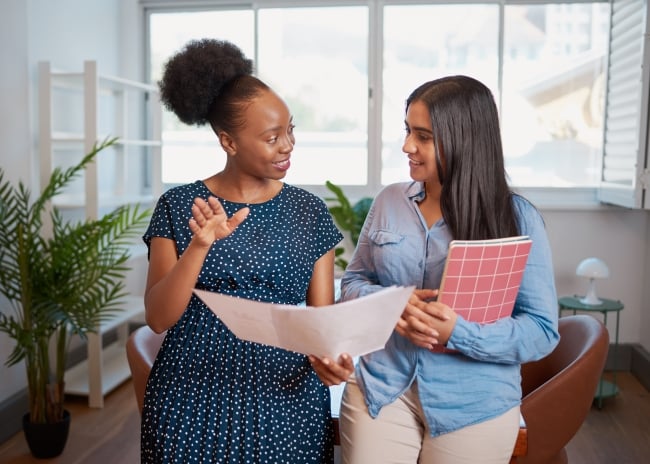 A photo of two women engaging in discussion in an office, suggesting the theme of mentorship and collaboration.