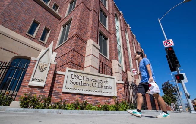 A student in a blue shirt walks past a brick campus building