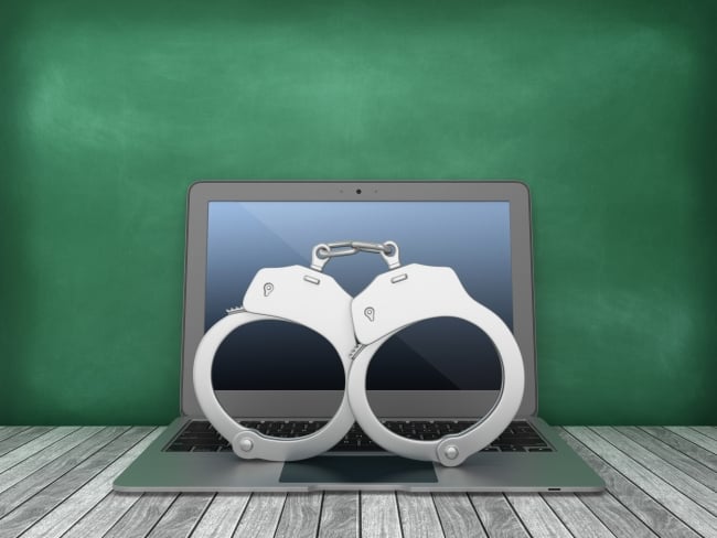 Computer with handcuffs on top of it sits in front of a blackboard
