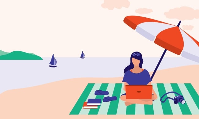 Woman sitting at beach working on computer with several books beside her