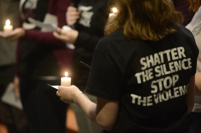 Students at a candlelight vigil, one wearing a shirt that says "Shatter the Silence, Stop the Violence"