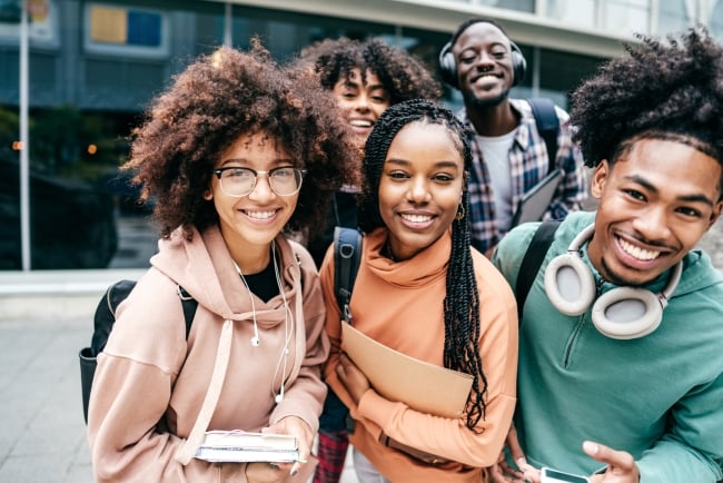A group of students smile while holding books and backpacks.