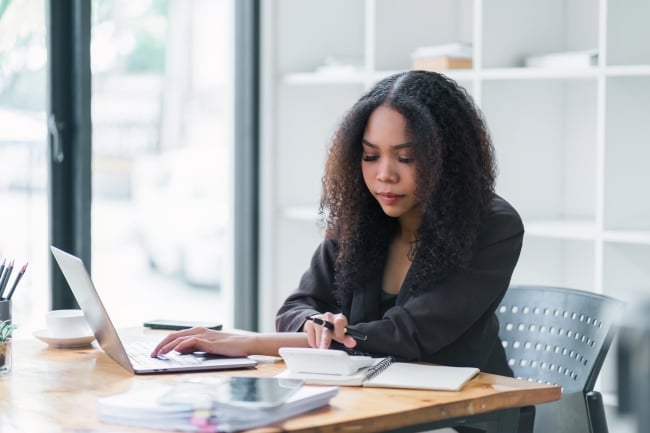 Businesswoman accountant using a calculator, graphs and charts to analyze market data, balance sheets, accounts and net profits in order to plan new sales strategies and increase production capacity