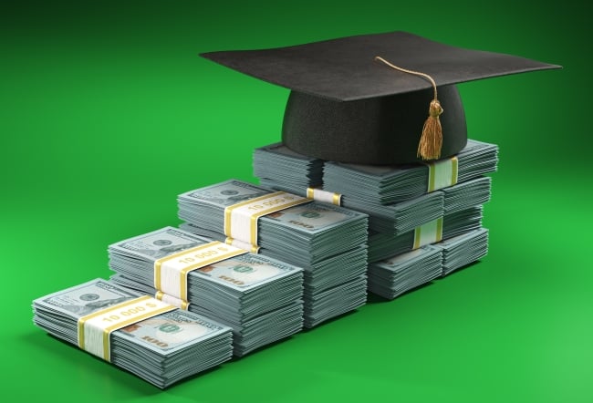 Stacks of U.S. dollars of different heights are lined up to create the impression of an ascending staircase; a graduation cap with tassel sits on the top level.
