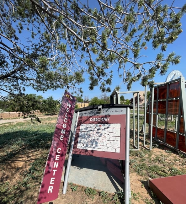 A maroon welcome sign and a campus directory with a map are heavily leaning, as in disrepair.