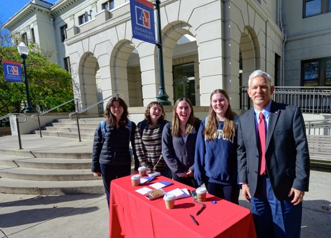 President Alger stands beside four AU students at a table outside on campus