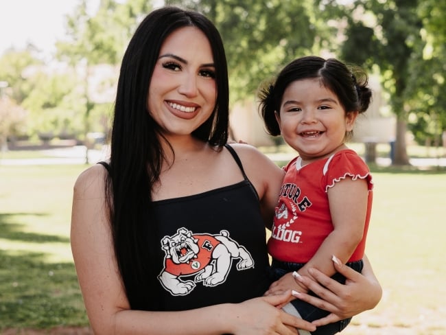 A mom and daughter smile in matching Fresno State gear on a sunny day