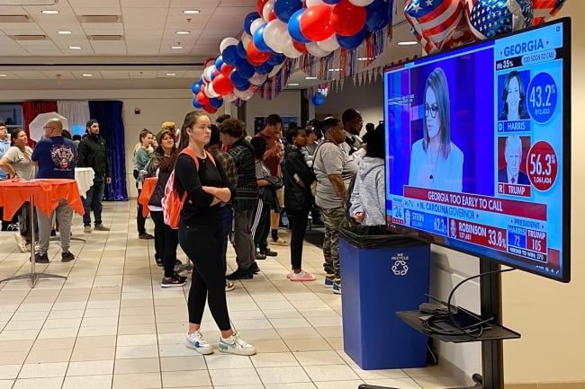 Students at Gallaudet University stand in a room next to a TV screen that shows Georgia as too early to call
