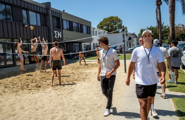 A group of students play volleyball outside of the Sigma Nu fraternity house while others walk on the sidewalk